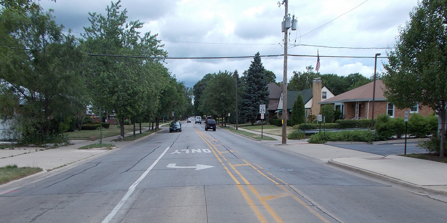 A street with cars driving down it and trees in the background.