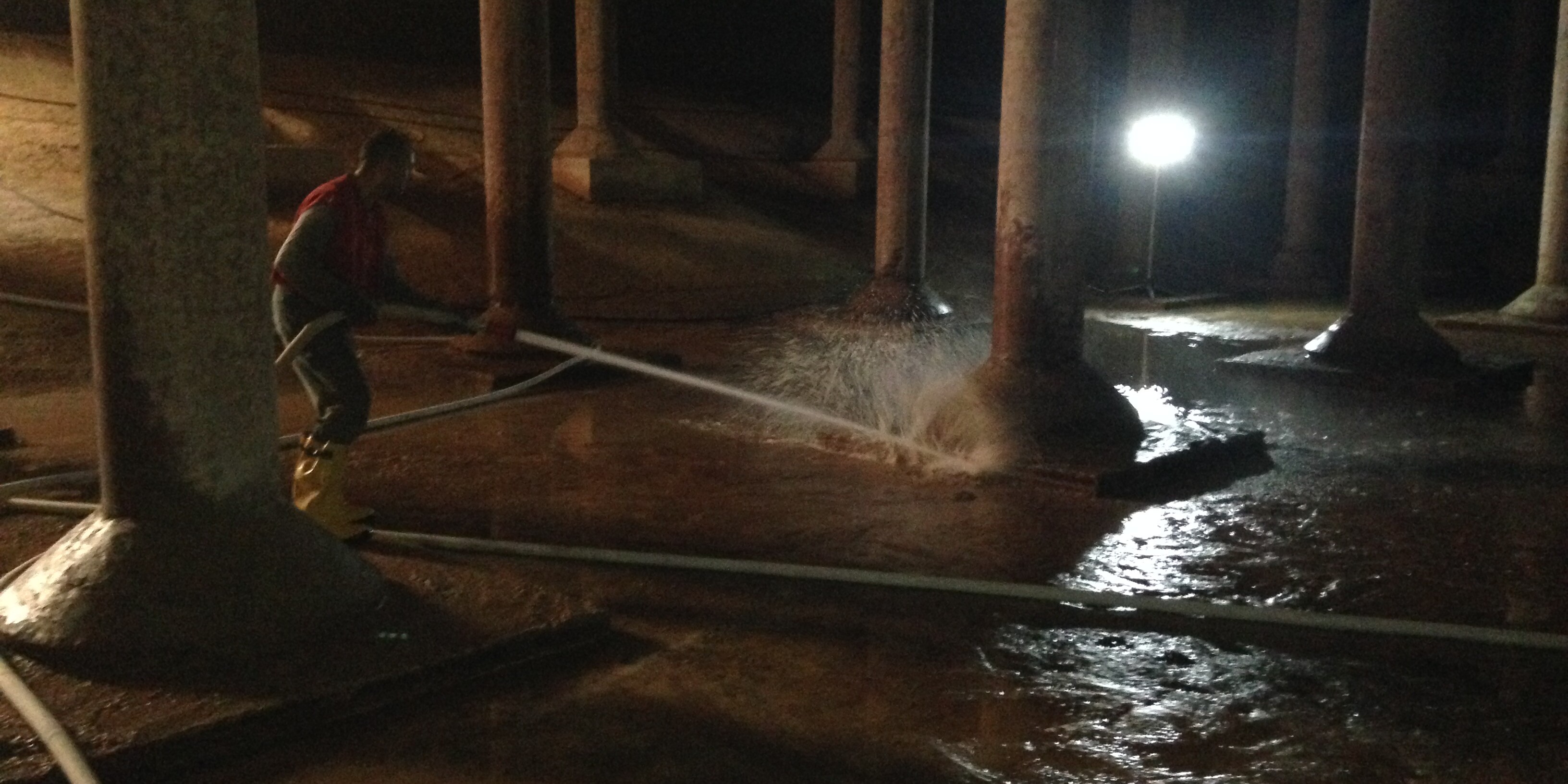 A man is spraying water from the floor of an underground tunnel.