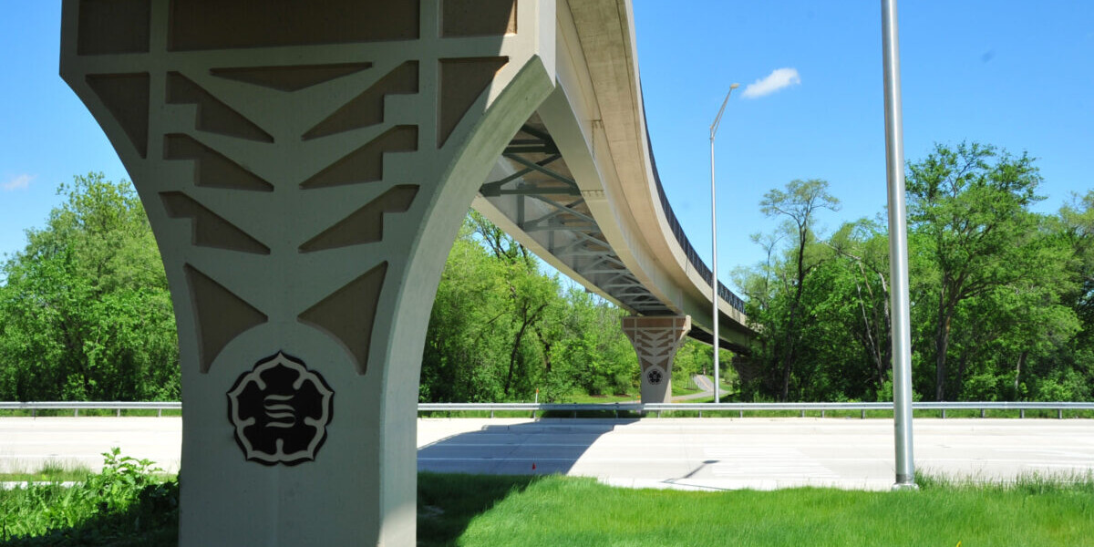 A bridge with trees in the background and grass on the ground.