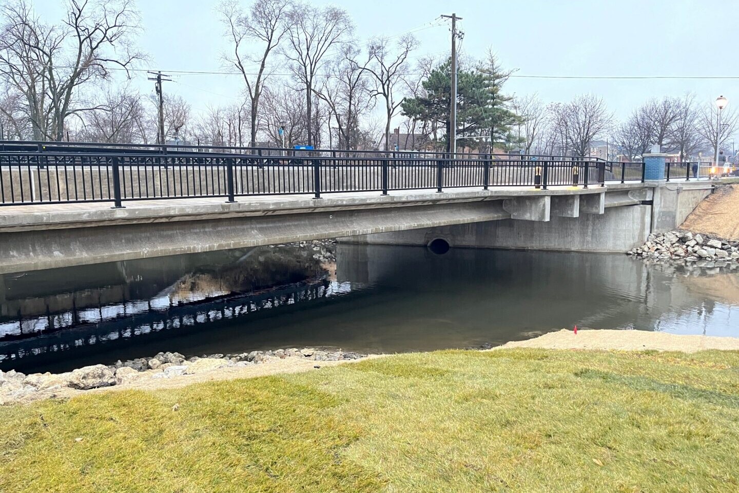 A bridge over the water with grass in front of it.