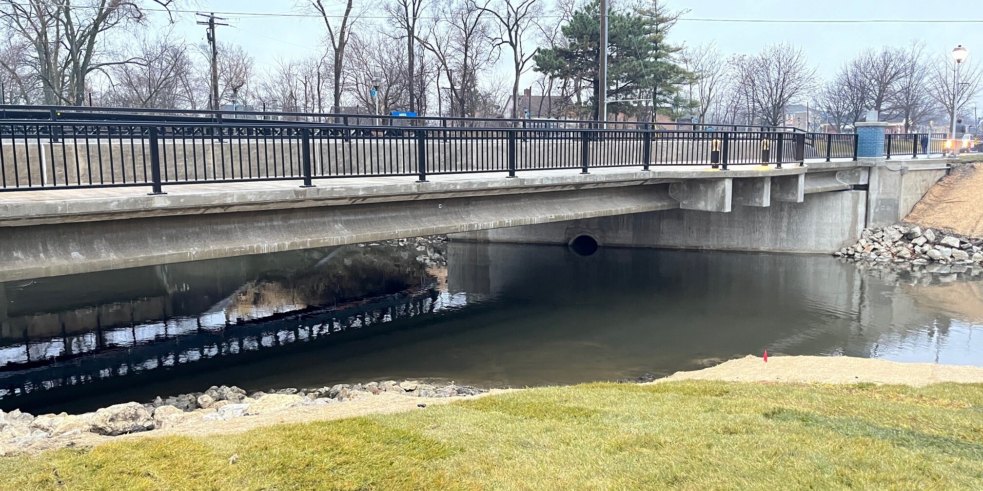 A bridge over the water with grass in front of it.